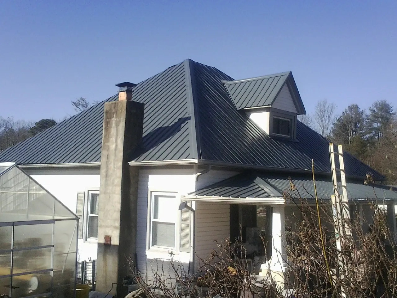 Dark blue standing seam metal roof on a white farmhouse with dormer — Slate & Tile Roof Repair by Roofing Brothers in Middle Amana