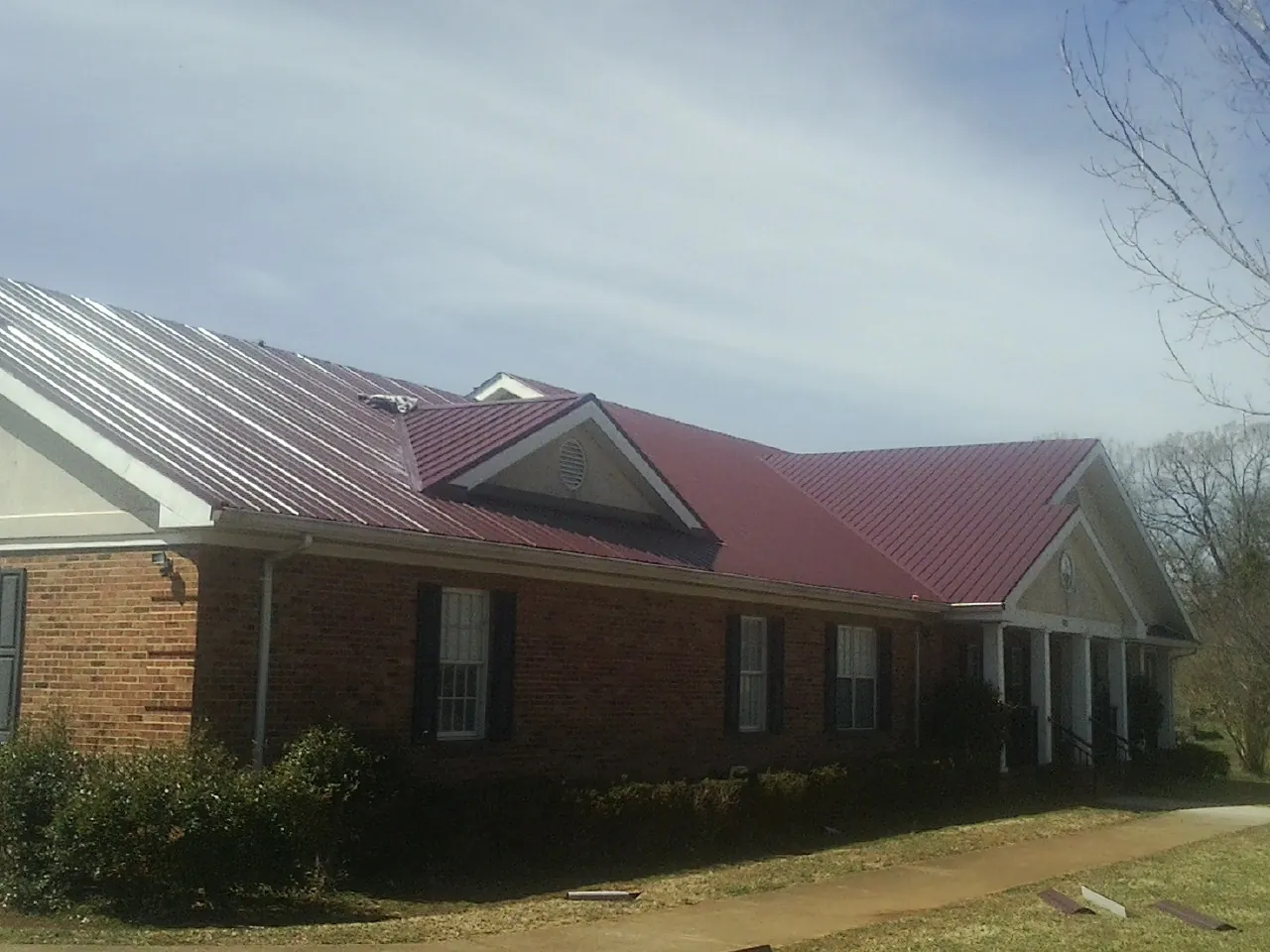 Red metal roof with gabled entries on a long brick building, from a Hail Damage Roof Repair job in Middle Amana