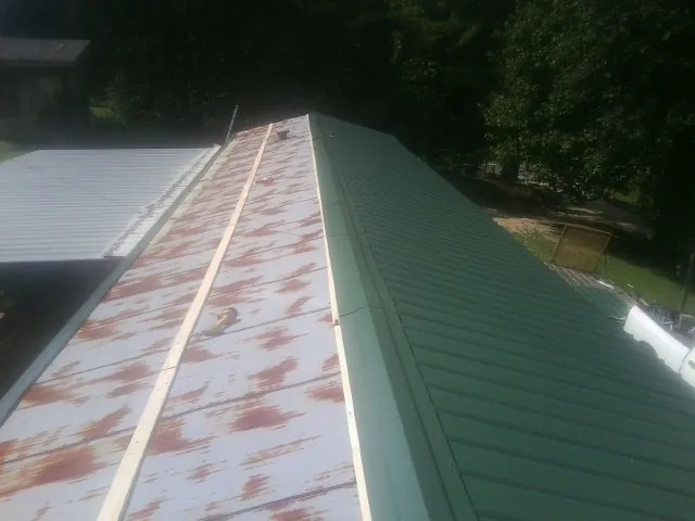 Old rusted panels beside newly installed green metal roofing — Wind Damage Roof Repair by Roofing Brothers in Middle Amana