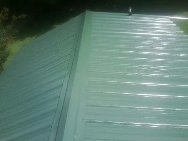 New green metal panels meeting at the ridge of a roof — Flat Roof Repair work by our crew in Middle Amana