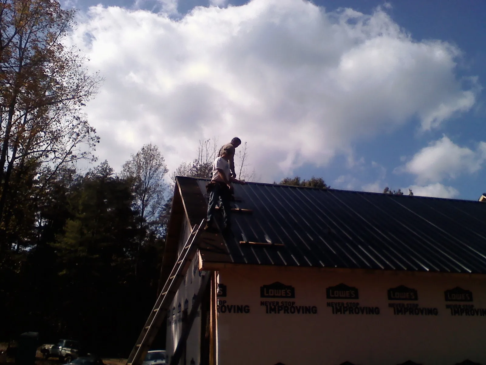 Roofer fastening dark metal panels high against a cloudy sky, from a Roof Inspection job in Middle Amana