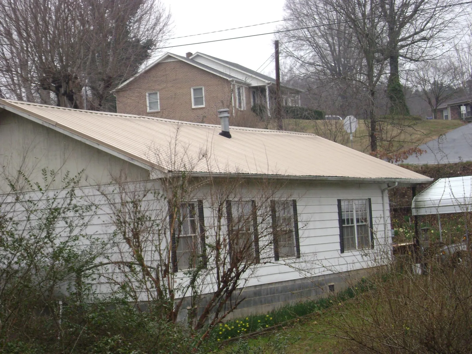 Tan metal roof on a white sided house set into a hillside — Commercial Roofing by Roofing Brothers in Middle Amana