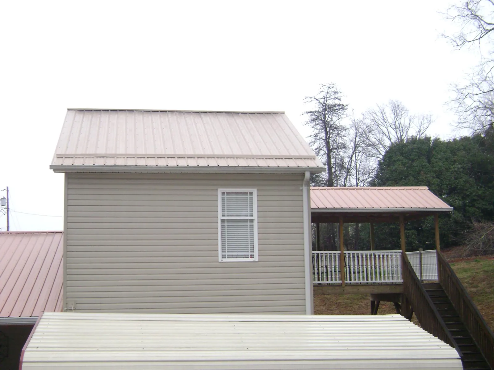 Tan metal roofs on a two story addition and attached porch, from a Roof Replacement job in Middle Amana